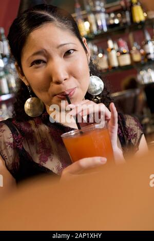 Giovane donna asiatica millenaria americana sorseggiando un drink in un bar locale Foto Stock