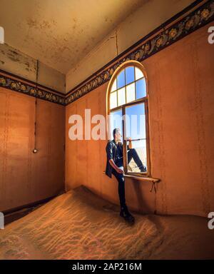 Tourist si trova nella finestra di una camera nella città fantasma Kolmanskop, Namibia Foto Stock