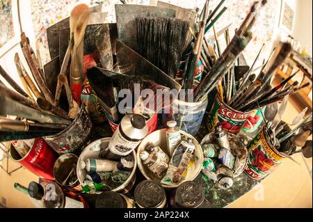 Una varietà di spazzole di vernice e la vernice in un consueto assortimento di contenitori nella parte anteriore di un artista tela nel suo studio Foto Stock