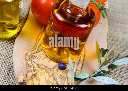 Italiano mediterraneo cibo sano concetto: isolato vicino fino di olio d'oliva bottiglie su legno tagliere con ramoscello e pomodori rossi Foto Stock