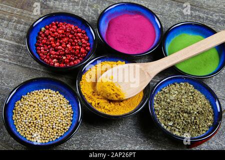 Vicino la vista dal di sopra su sei ciotole blu con varie spezie colorate in polvere e grani sul tavolo di legno. Cucchiaino di curcuma curcuma ciotola. Foto Stock