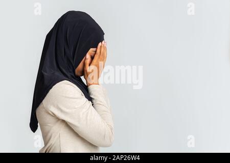 Ritratto di profilo di disperati nero donna musulmana che ricopre la faccia con le mani Foto Stock