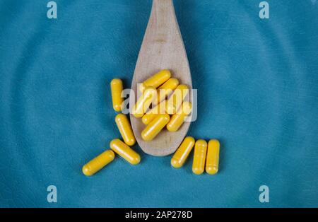 Integratore alimentare e nutrizione sana nozione: Chiusura del cucchiaio di legno con palo di capsule di colore giallo su blu graffiato la piastra di cina Foto Stock