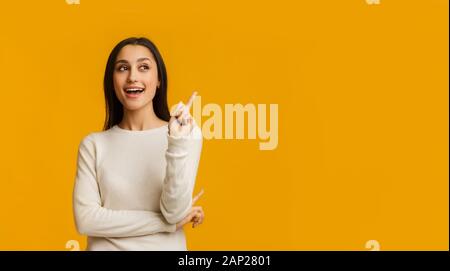 Bruna giovane donna puntare il dito verso l'alto avendo idea su sfondo giallo Foto Stock