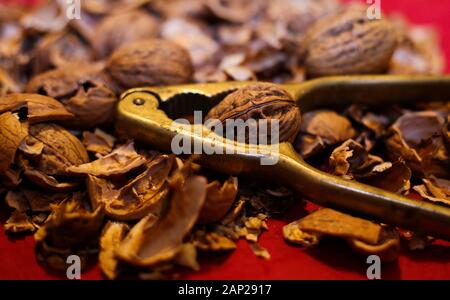 Vicino la pila con incrinato i gusci di noce e isolato leva retrò schiaccianoci con sfondo rosso. Foto Stock