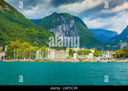 Riva del Garda porto con barche situato presso il lago di Garda, alte montagne sullo sfondo, giornata di sole Foto Stock