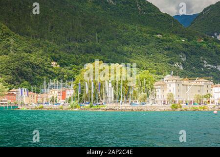 Riva del Garda porto con barche situato presso il lago di Garda, alte montagne sullo sfondo, giornata di sole Foto Stock