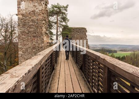 Uomo fotografo turistico tenere la fotocamera camminando sul vecchio ponte di legno in autunno. Ponte di Legno e Old Castle. Foto Stock