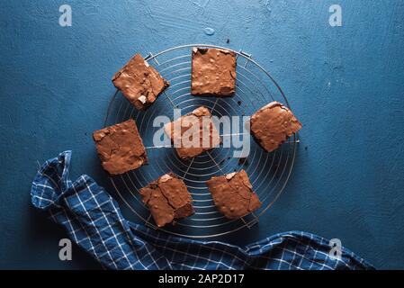 Pane appena sfornato dark brownie al cioccolato su una griglia di raffreddamento sul classico tavolo blu e carta asciugatutto. Il miglior brownies dessert. Torta al cioccolato piazze. Foto Stock