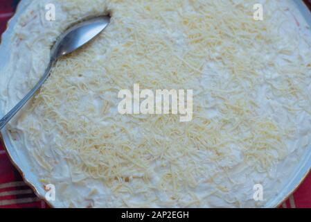 Deliziosa la Mimosa insalata di patate, sardine, cipolle, uova, carote, formaggio in una piastra su un tavolo. Insalata di formaggio grattugiato Uova con maionese Foto Stock