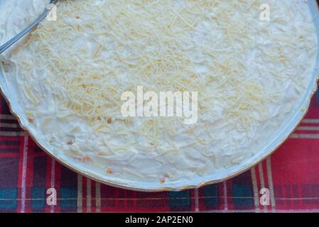 Deliziosa la Mimosa insalata di patate, sardine, cipolle, uova, carote, formaggio in una piastra su un tavolo. Insalata di formaggio grattugiato Uova con maionese Foto Stock