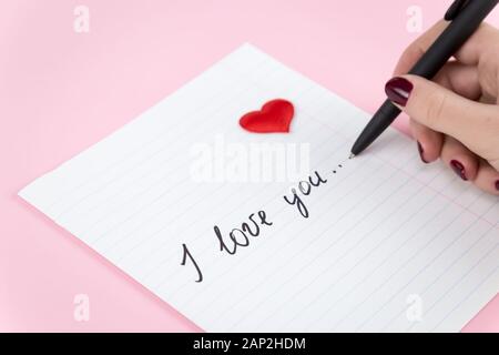 Mano femminile comporta la scrittura di una dichiarazione di amore su carta Foto Stock