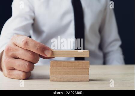 Vista frontale di un imprenditore vuoto di impilamento picchetti di legno in una immagine concettuale. Foto Stock