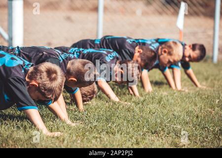 Gruppo di giovani calciatori eseguire warm-up prima di esercizi di allenamento di calcio. I giovani giocatori facendo push-up esercizi all'aperto. Foto Stock
