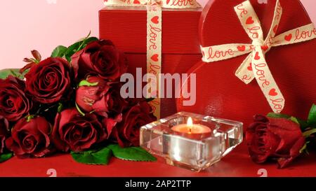 Happy regali di San Valentino e rose rosse sul rosso e sfondo rosa. In prossimità della messa a fuoco sulla candela accesa. Foto Stock