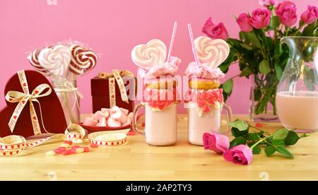 Sul trend il giorno di San Valentino messa in tavola con Fragola Rosa freak scuote e rabboccato con a forma di cuore ad lecca-lecca, ciambelle e caramella di cotone. Ampia crop per noi Foto Stock