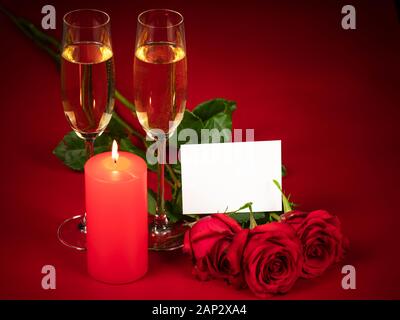 Close-up di tre rose rosse, due bicchieri di champagne e una accesa candela rossa su uno sfondo di colore rosso in onore di san valentino, giorno di nozze, anniversario. Foto Stock