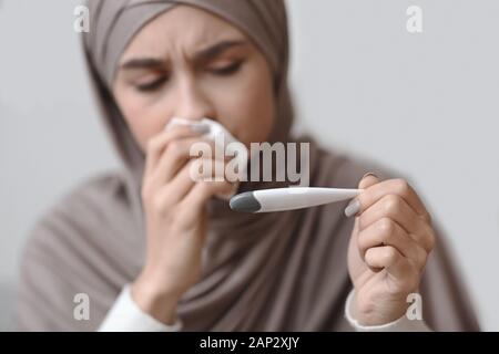 Malati donna araba in velo tenendo il termometro e soffiare il naso che cola Foto Stock