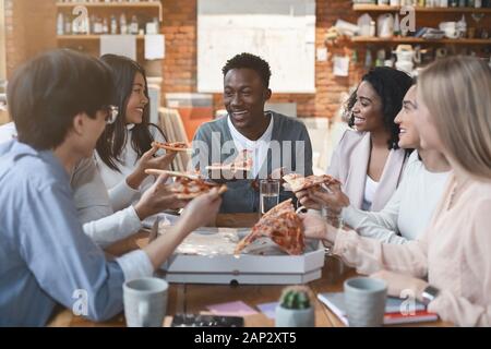 Le persone felici di mangiare il pranzo a coworking office durante l'interruzione Foto Stock