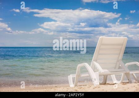 Sul lato destro di plastica piccola sedia a sdraio in piedi sulla sabbia di una spiaggia contro il mare. Bella blu cielo sopra il mare. Foto Stock