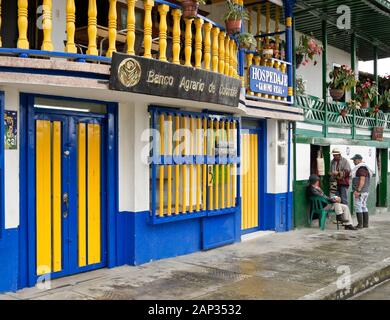 Gli uomini la socializzazione al di fuori colorati edifici coloniali (banca, hotel, piccolo negozio) nel triangolo di caffè città del Salento, dipartimento di Quindio, Colombia Foto Stock