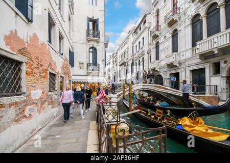 Una sezione di occupato di canal in Calle de la Canonica come turisti attraversare il ponte su una gondola e un gondoliere attende i clienti a Venezia, Italia Foto Stock
