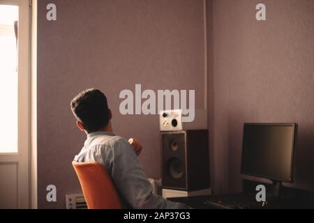 Uomo che guarda attraverso la finestra mentre si siede accanto al computer desktop Foto Stock