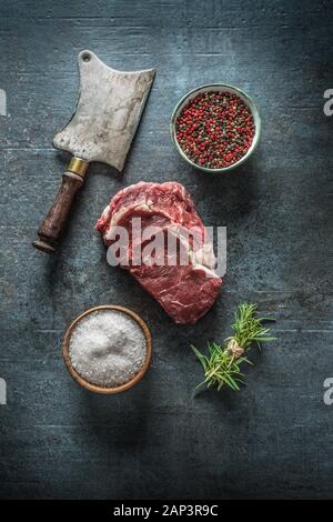 Raw bistecche di manzo con carne cleaver e sale pepe su scuro dello sfondo in calcestruzzo Foto Stock