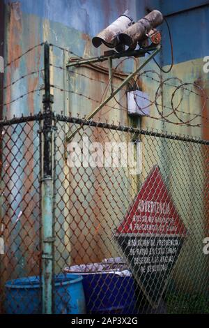 Telecamere di sorveglianza in cima a una recinzione di maglia di catena che circonda un edificio arrugginito e vecchio. Foto Stock