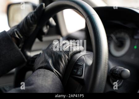 Mani di guida in guanti di pelle che soffiano l'avvisatore acustico premendo verso il basso sul volante della vettura`s. Foto Stock