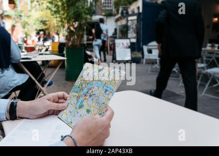 Donna turista tiene una mappa della città in una zona commerciale alla moda seduta su una terrazza Foto Stock