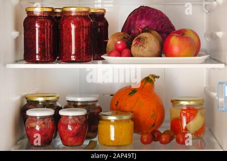 Vasetti con frutta fatta in casa e marmellate di frutti di bosco e verdure fresche rosse, viola e arancioni e frutta a scaffale in frigorifero. Cibi vegetariani sani fermentati Foto Stock