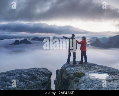 Gli amanti il mirroring in acqua occhio al vertice di montagna al di sopra di una nebbia fitta. Coppia di arrampicata in cima alla vetta con incredibile vista aerea Foto Stock
