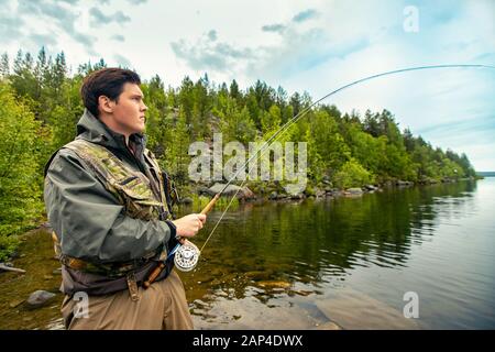 Pescatore che utilizza pesca con la mosca della canna nel fiume di montagna che spruzzano l'acqua Foto Stock