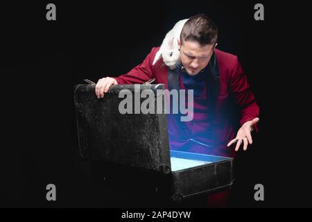 Il mago mostra trucco con scomparsa coniglio bianco in valigia Magic wand, sfondo nero Foto Stock