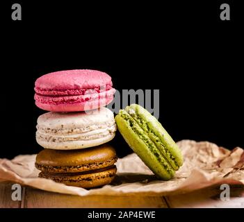 Retrò pastello colorati amaretti su sfondo nero con copyspace. Dolce di macaron francese fatto in casa con diversi sapori: Cioccolato, cannuccia Foto Stock