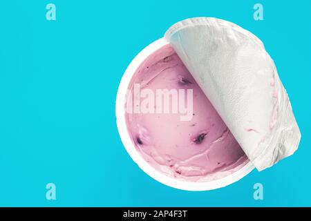 Uno yogurt rosa con mirtillo in una tazza di plastica aperta su sfondo blu. Vista dall'alto, spazio di testo Foto Stock