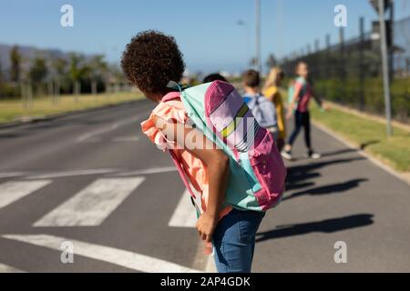 Scolaresche che cercano traffico in attesa di attraversare la strada Foto Stock