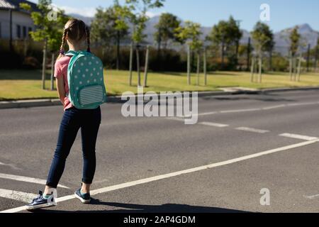 Scolaretta alla ricerca di traffico in attesa di attraversare la strada Foto Stock