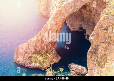 Grotta Azzurra A Malta. Una barca da diporto con i turisti. Finestra ad arco naturale in roccia Foto Stock