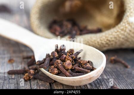 Una spezia di chiodi di garofano secchi si trova su un cucchiaio di legno ed è sparsa su vecchie tavole di legno vicino alla borsa. Spezie chiodi di garofano per cucinare. Primo piano. Foto Stock