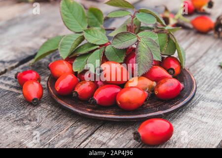 Freschi fianchi di rosa rossa e foglie verdi su una ciotola su un tavolo di legno. Primo piano. Foto Stock