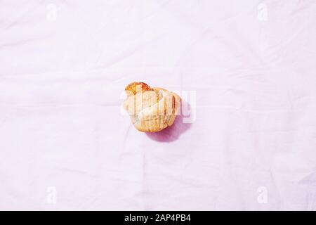 Pasticceria moderna alla moda cruffin (croissant e Muffin) con cannella e zucchero su sfondo tessile rosa pastello. Concetto di colazione o brunch Foto Stock