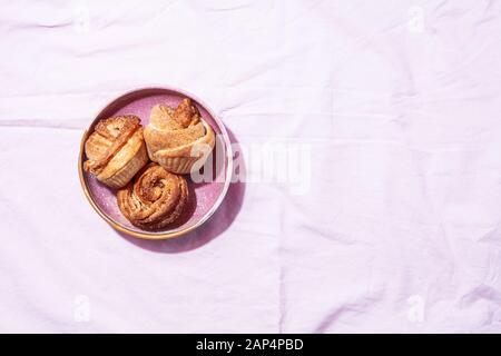 Pasticceria moderna alla moda cruffins (croissant e Muffin) con cannella e zucchero su piastra e sfondo tessile rosa. Concetto di colazione o brunch Foto Stock