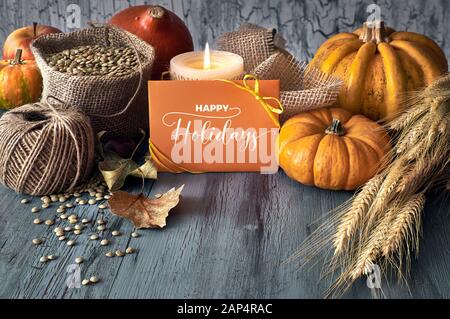 Autumn harvest ancora in vita con zucche, spighe di grano e lenticchie di sacco sacco con cavo, candela e scheda su grigio sfumato in legno rustico sfondo. P Foto Stock