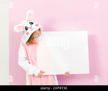 Bella ragazza bionda con un intimo costume di coniglio e segno bianco è in posa in studio ed è felice Foto Stock