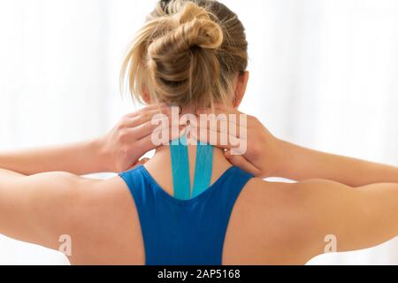 I giovani sportivi atleta femminile di toccare il suo collo ferito dopo trattamento con kinesio tape. Vista posteriore vicino. Kinesiologia, terapia fisica, rehabili Foto Stock