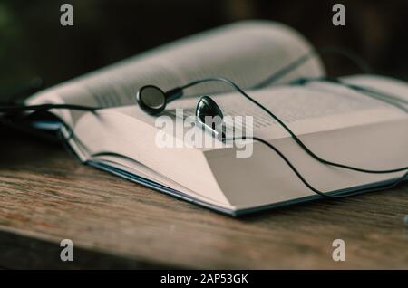 Aprire il libro sul tavolo. Le cuffie personali sono in alto. Vista laterale. Riprese a livello oculare. Messa a fuoco selettiva. Sfondo sfocato. Senza persone. Foto Stock