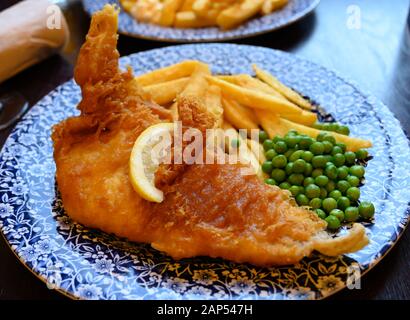 Tradizionale cibo britannico pesce e patatine servito con piselli verdi in pub Foto Stock