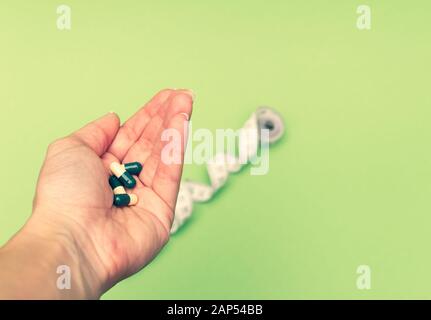 Pillole di dieta nella mano della donna e misuratore di misurazione su sfondo verde. Perdita di peso concetto. Foto Stock